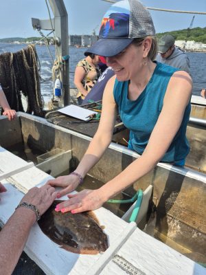 A woman measures a flounder on the back of a research boat.